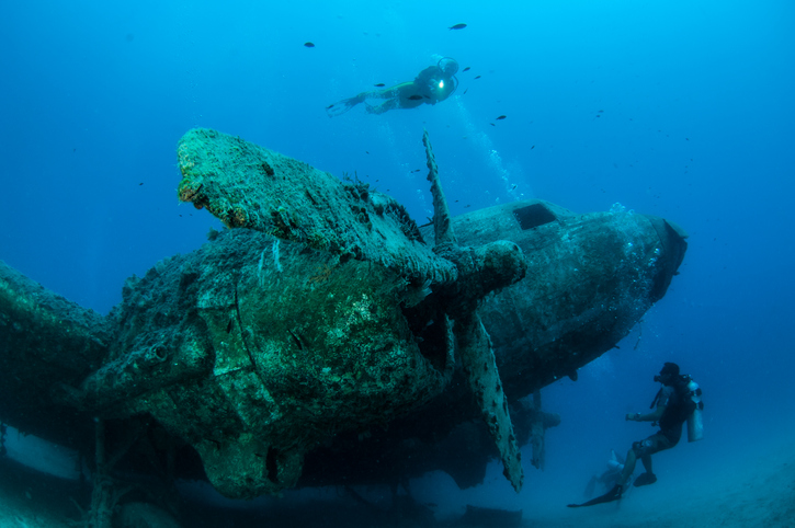 wrecked plane under water with scuba diver nearby