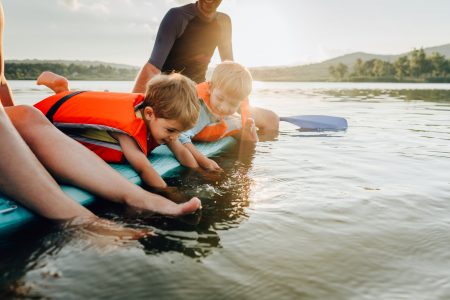 Photo of two cute brothers and their parents paddling on the lake, and enjoying summer days far from the hustle of the city.